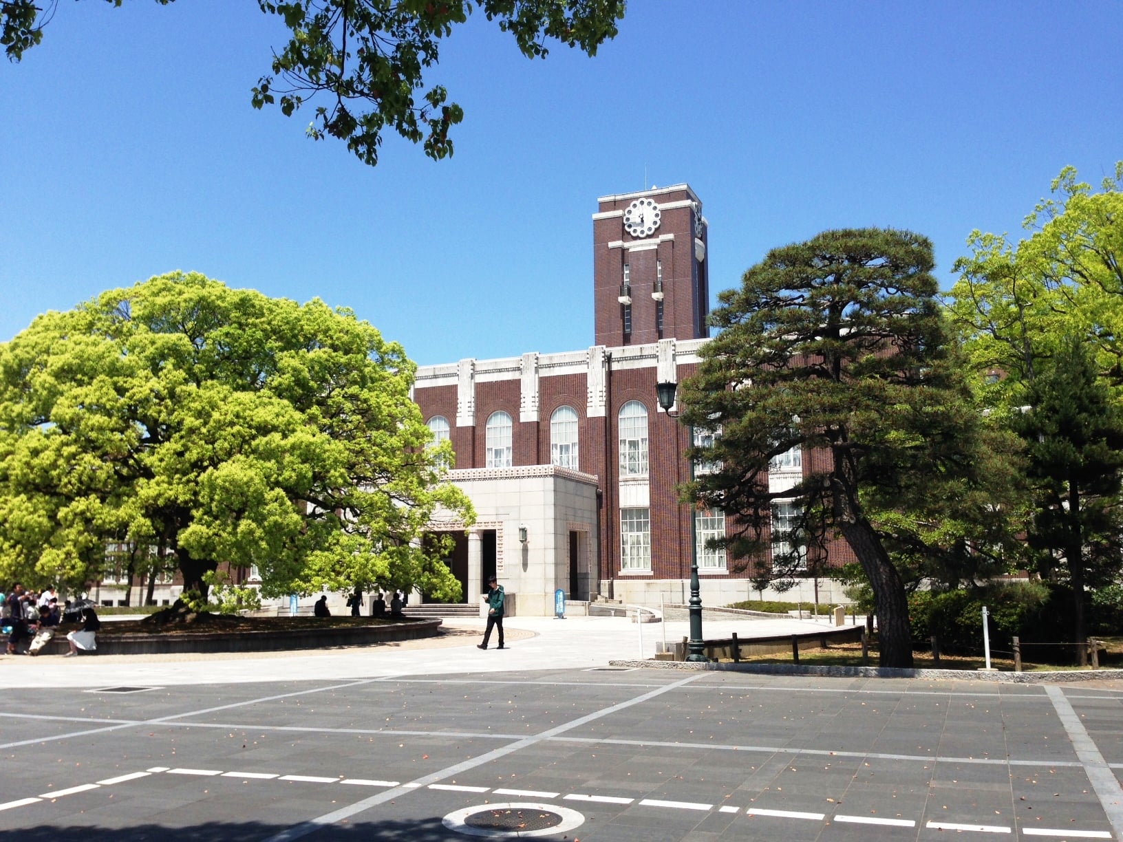 The red-brick clock tower of Kyoto University behind a large camphor tree
